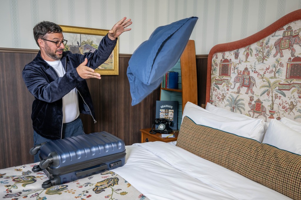 Simon Bird throwing a pillow onto the bed at Graduate by Hilton Cambridge - Graduate by Hilton - The Great Travel Debate