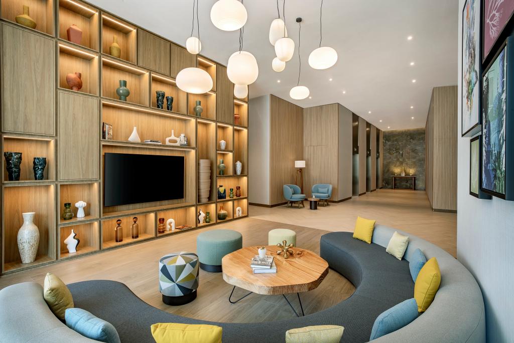 Hilton Garden Inn Dubai Business Bay - Lobby with large circular couch and table seating area, and television wall with art pieces