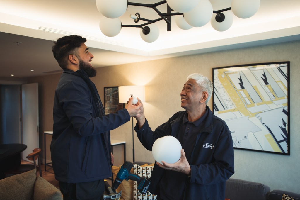 Two men changing a light bulb in a chandelier in hotel room