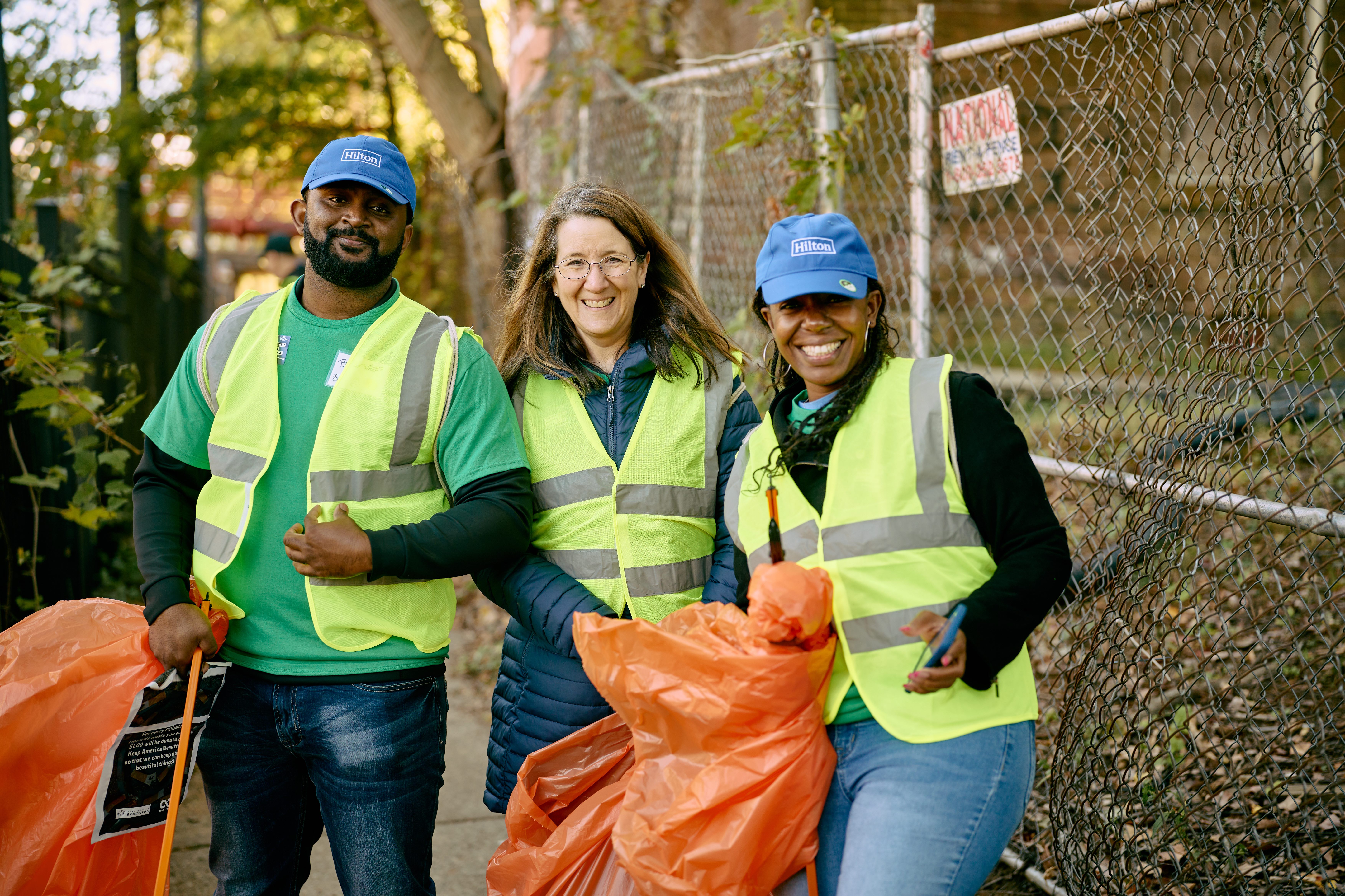 three volunteers wearing Hilton blue caps, safety vests and holing orange garbage bags