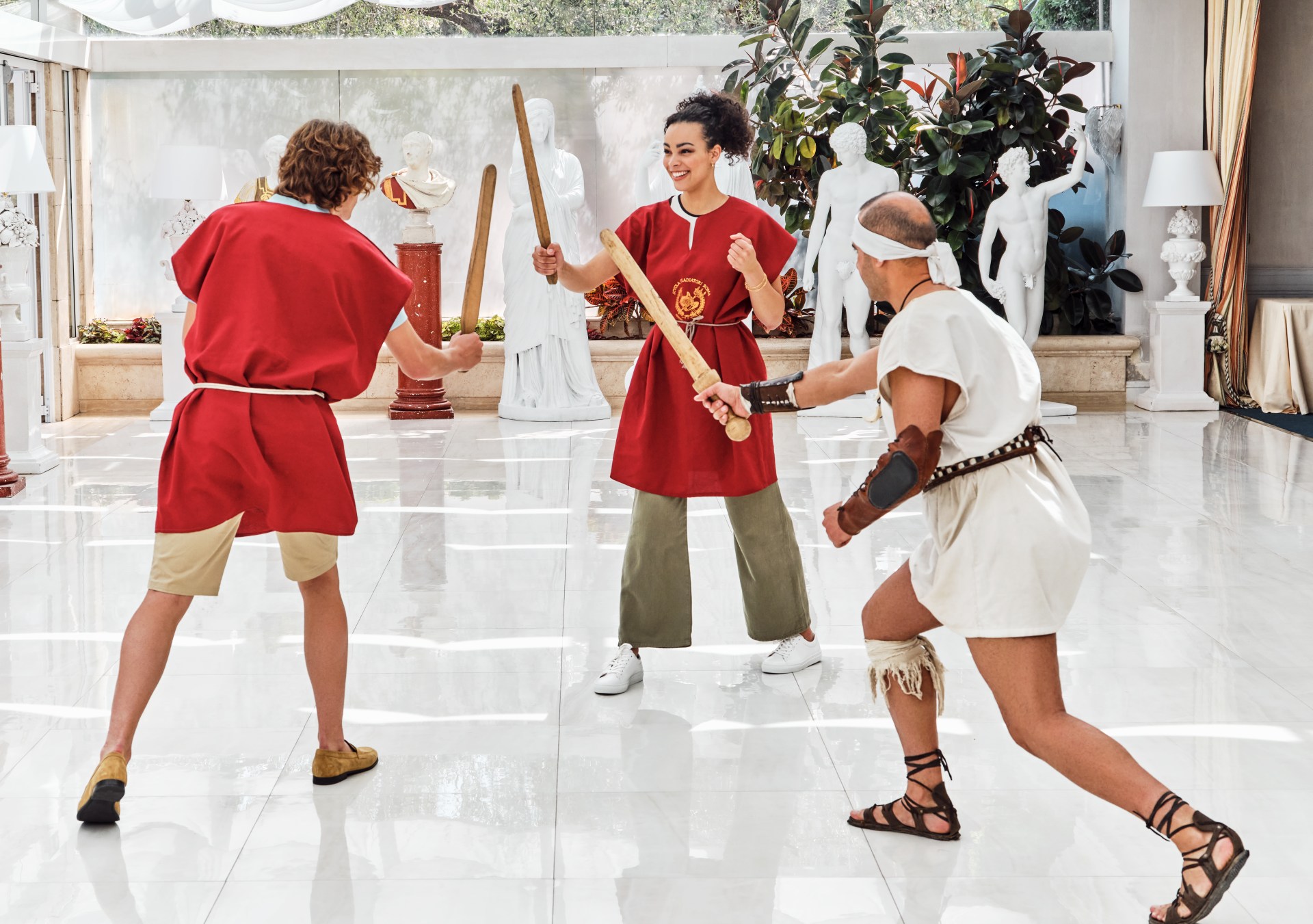 Couple in gladiator training experience with trainer, wooden swords, statuary surrounding area