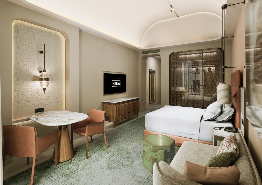 Hilton Cairo Historic City, sitting area, guest room, bed, television, sconce lighting, mirror with light, green coffee table, couch, marble nightstand, leather chairs, leather headboard, green carpet