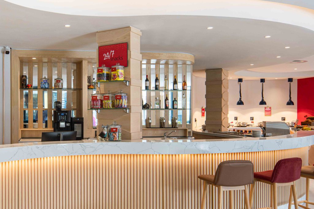 Hampton by Hilton Sandton Grayston - Bar area, bar stools, snacks and drinks behind the bar, self-service food bar in the background