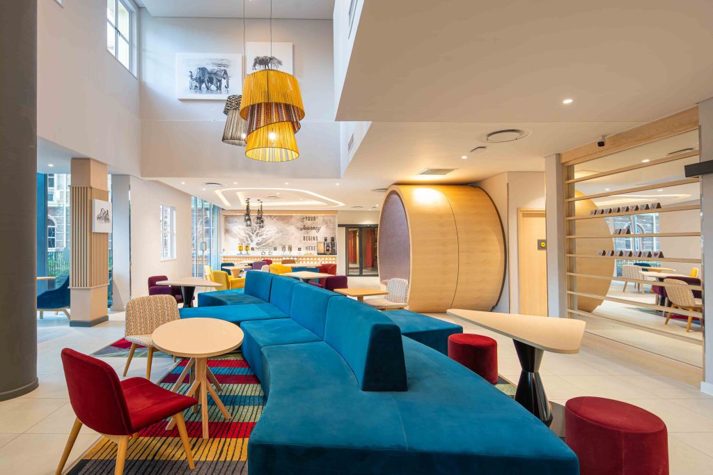 Hampton by Hilton Sandton Grayston - Resturant, large blue couch surrounded by table and chairs.