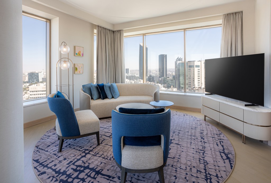 Signia by Hilton Amman, living room area with couch, chairs and tv on console, view of the city