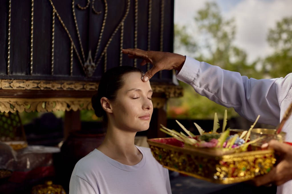 Umana Bali, LXR Hotels &amp; Resorts, Cultural ceremony with person applying marking on another persons forehead