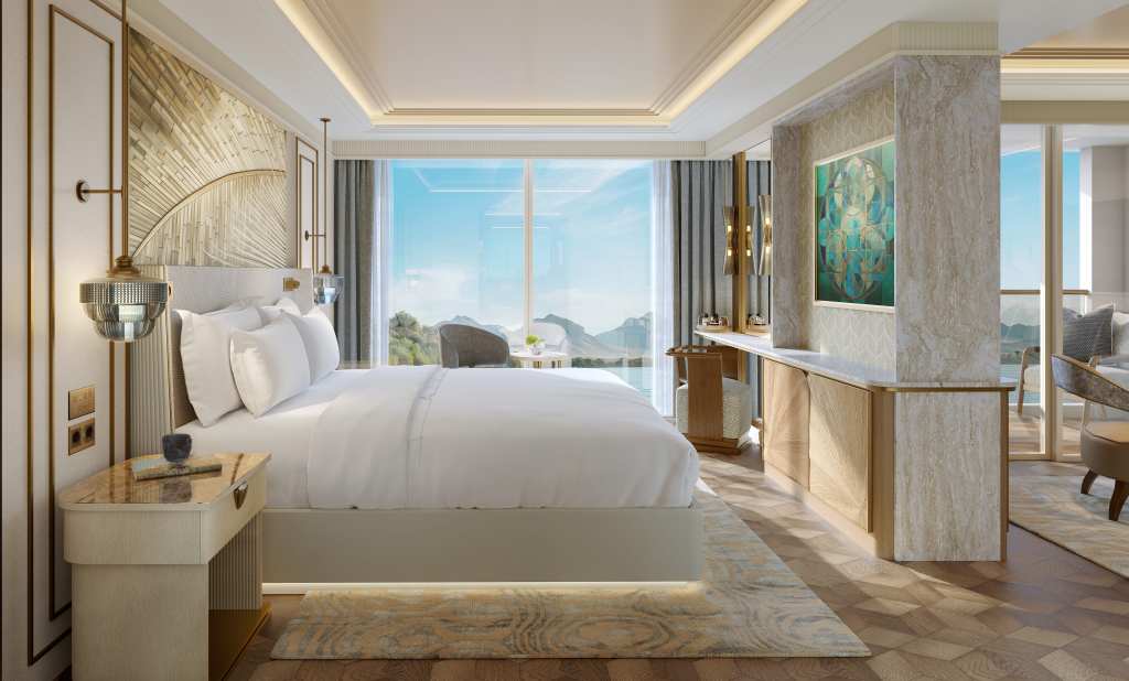 Bedroom with a bed with side tables that have lights above them with a view from a window that has lounge seating next to it, wall with wooden doors and a framed hanging artwork, balcony with lounge seating, area rugs on wood designed flooring