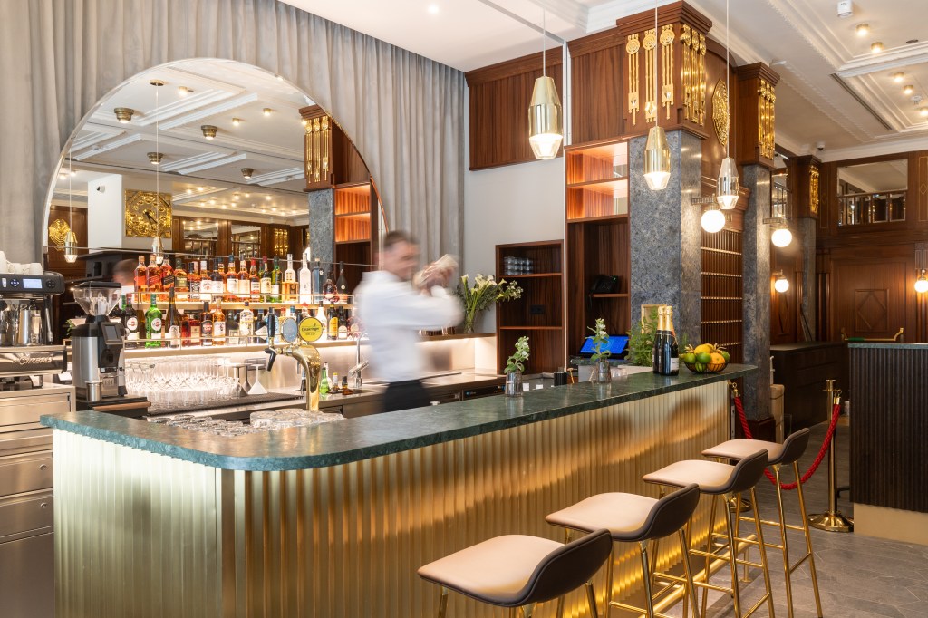 Bar with arched mirror backdrop and a bartender shaking a cocktail in behind bar with bar with four stools