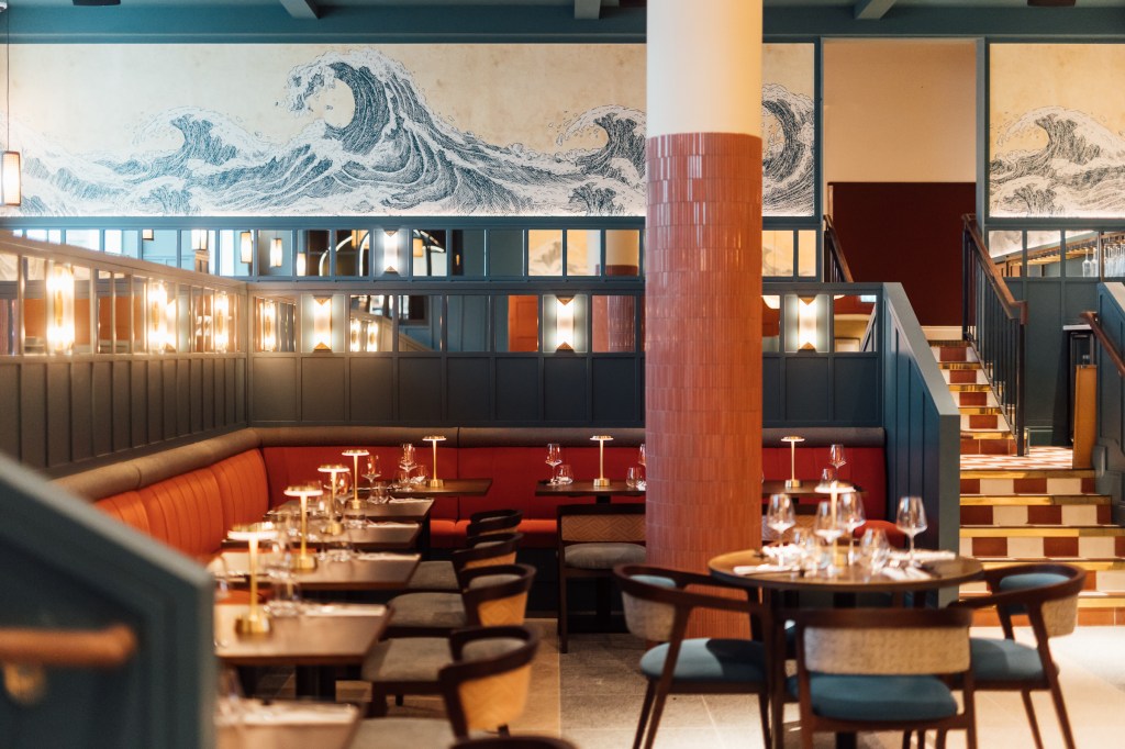 Restaurant dining room with black tables set for dinner and wave artwork and mirrors on the wall at The Marcus Portrush, Tapestry Collection by Hilton -