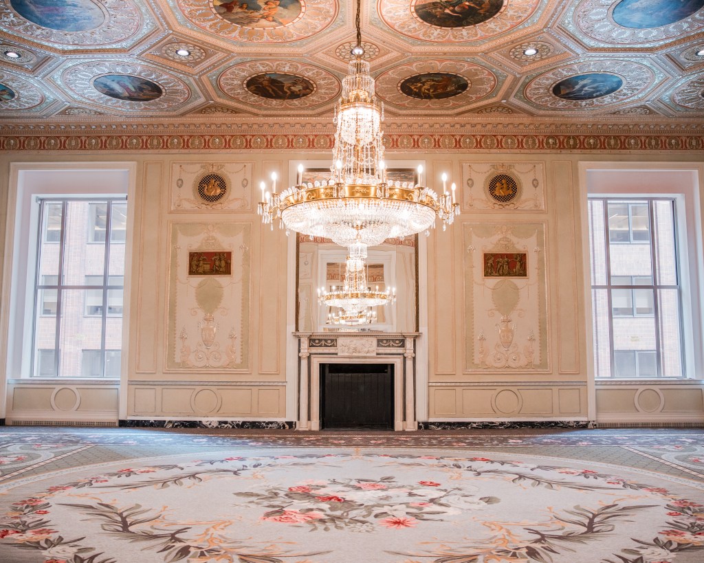 Waldorf Astoria New York Basildon Fireplace - Credit Waldorf Astoria New York, large carpeted room with chandelier and fireplace