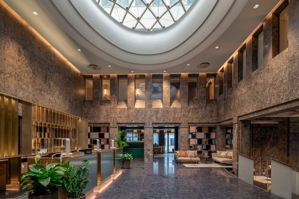 Hilton Turin Centre Front lobby Desk area with skylight, welcome desk, small seating area and view of dining area in background