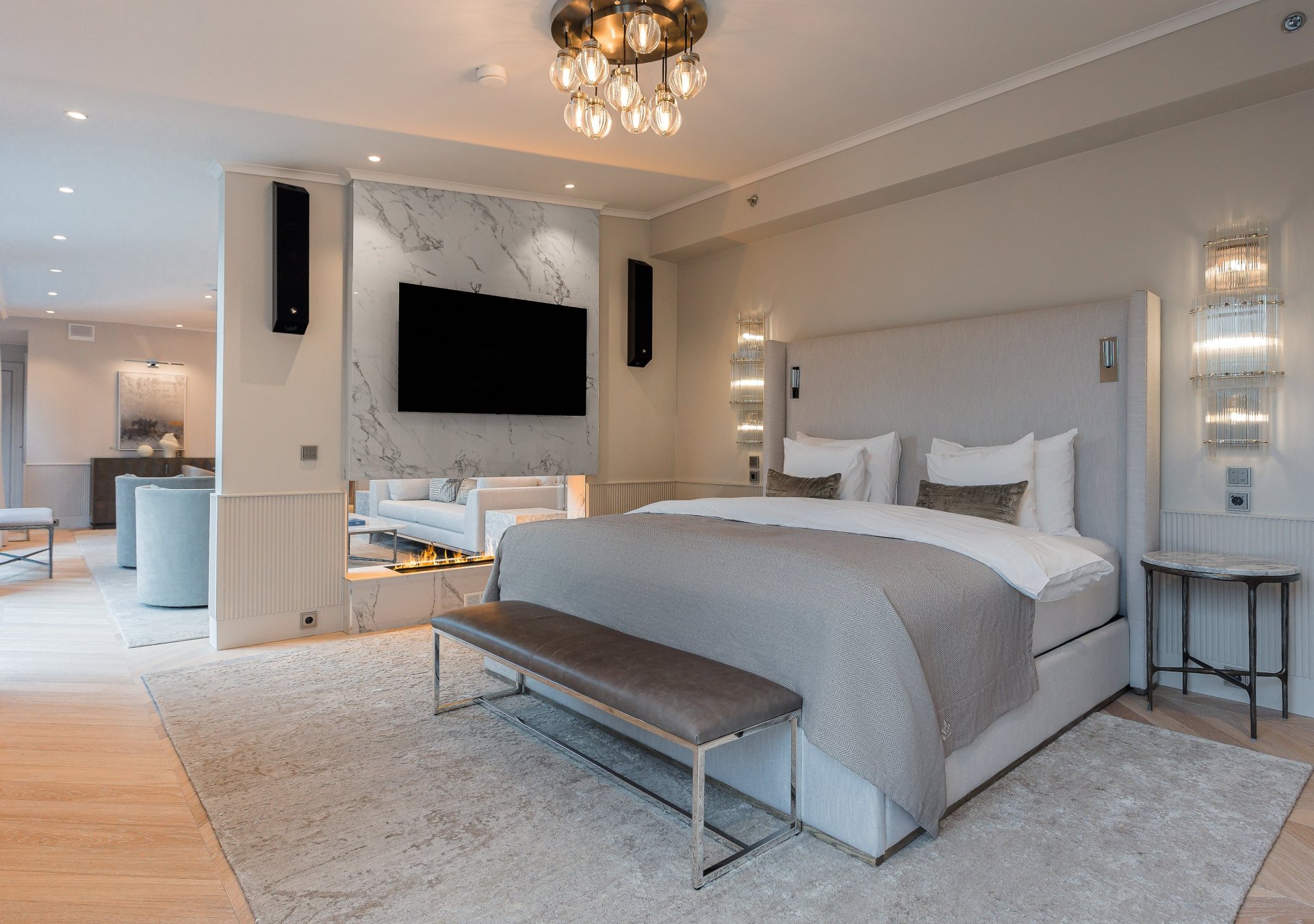Waldorf Astoria Helsinki - Penthouse Suite Bedroom, silver, marbel and brown leather decor,tv and speaker system over fireplace, bed with bench at the foot, side tables and sconces, view of living room in background
