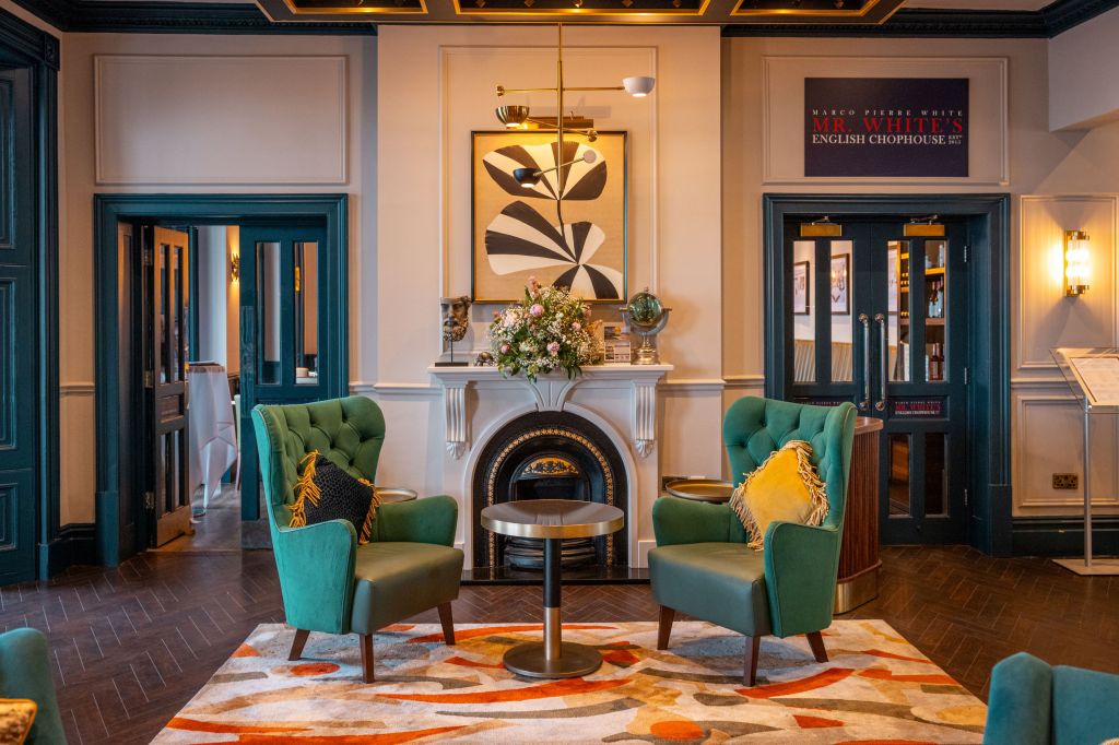 A seating area with green wingback chairs in front of a fireplace in the lobby of the Dover Marina Hotel &amp; Spa