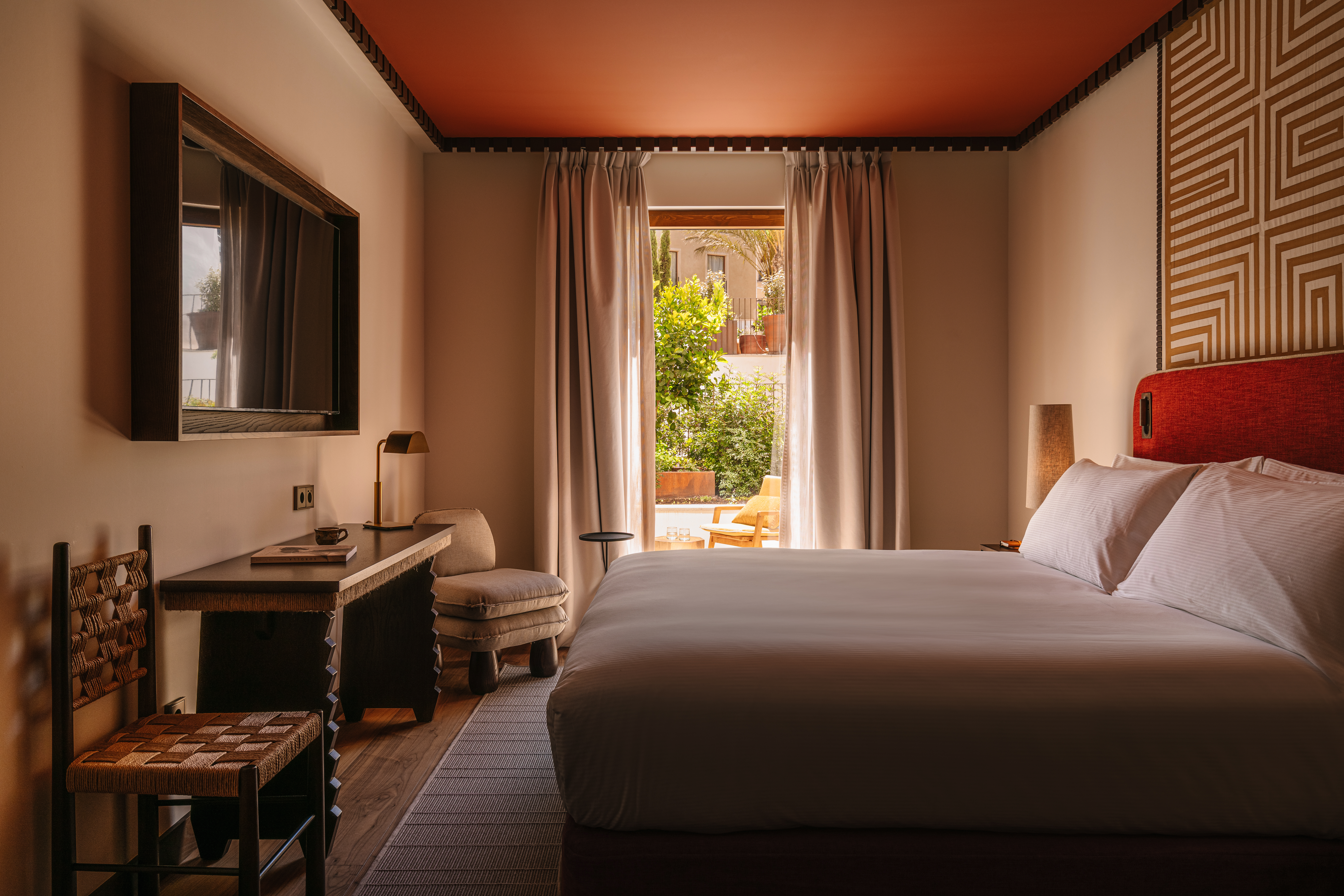 Bedroom with king bed, two chairs, and TV, overlooking with an outdoor seating area in the background
