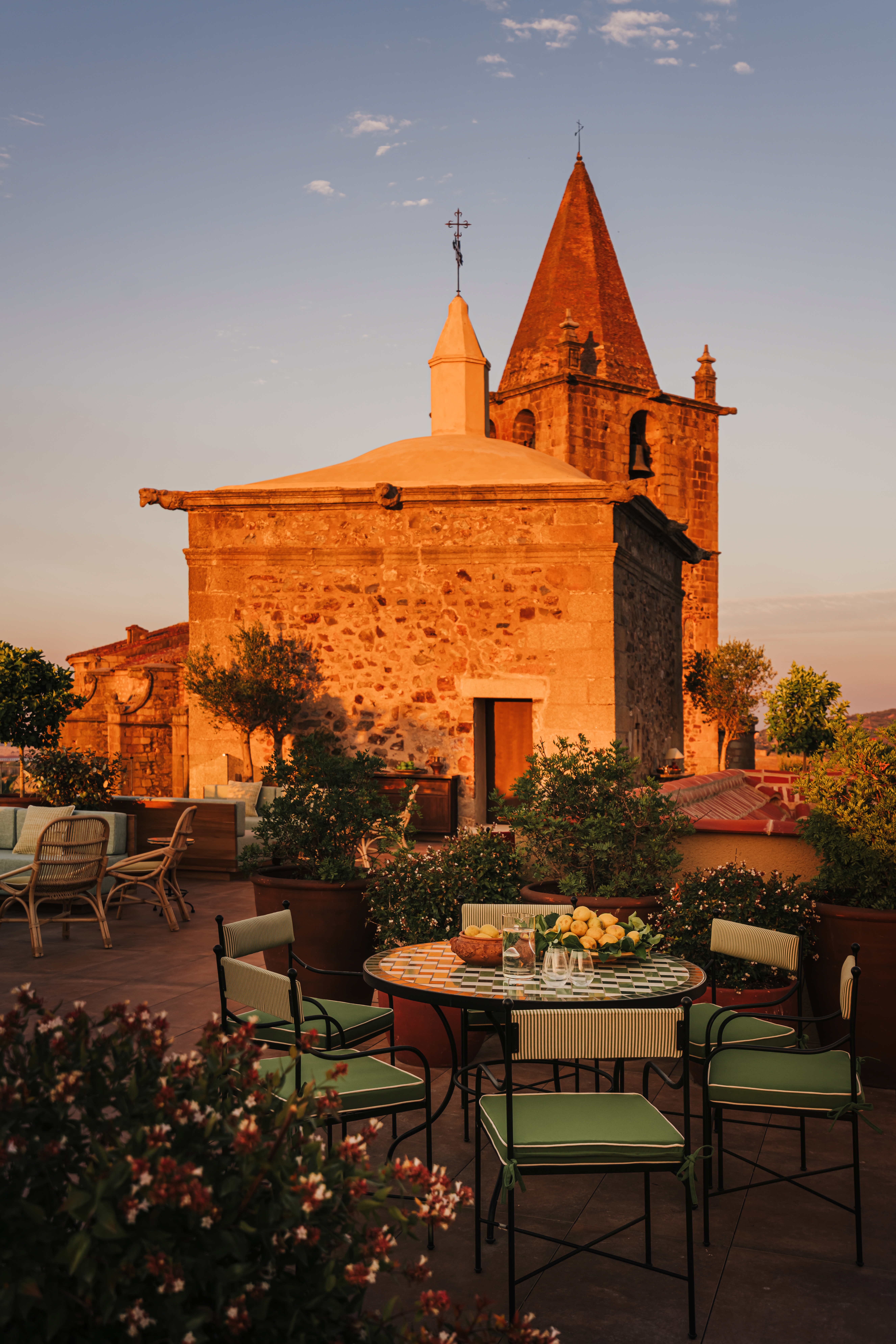 A terraza outside the Palacio de Godoy Caceres lit by beautiful evening light, with a table and chairs in the foreground, and other seating in the background.