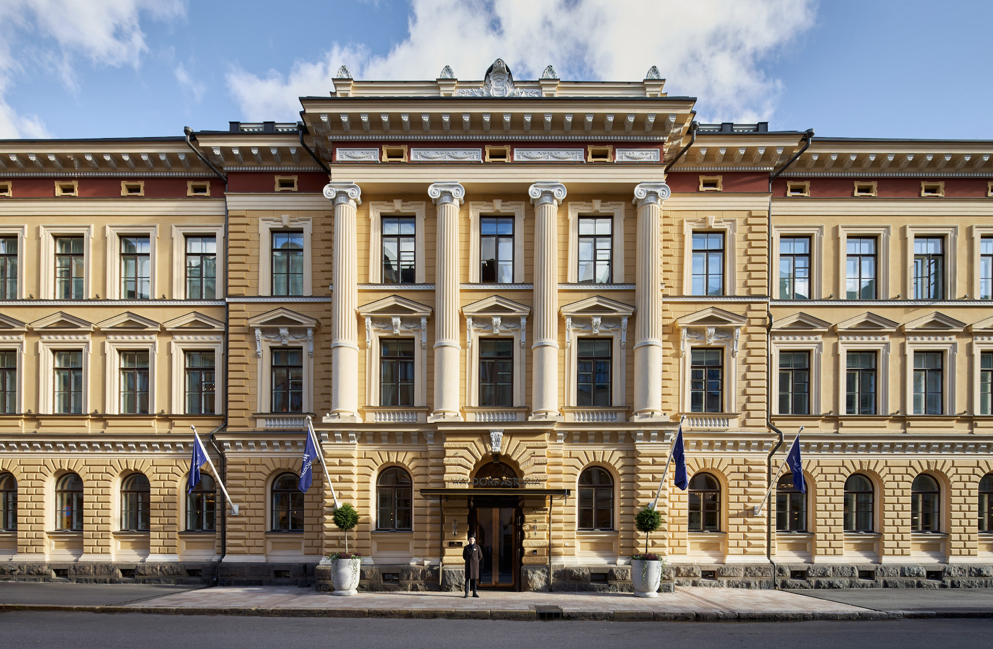 Front exterior of Waldorf Astoria Helsinki with columns and flags.