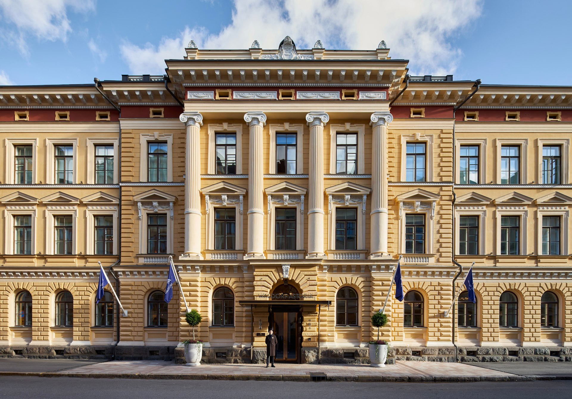 Front exterior of Waldorf Astoria Helsinki with columns and flags.
