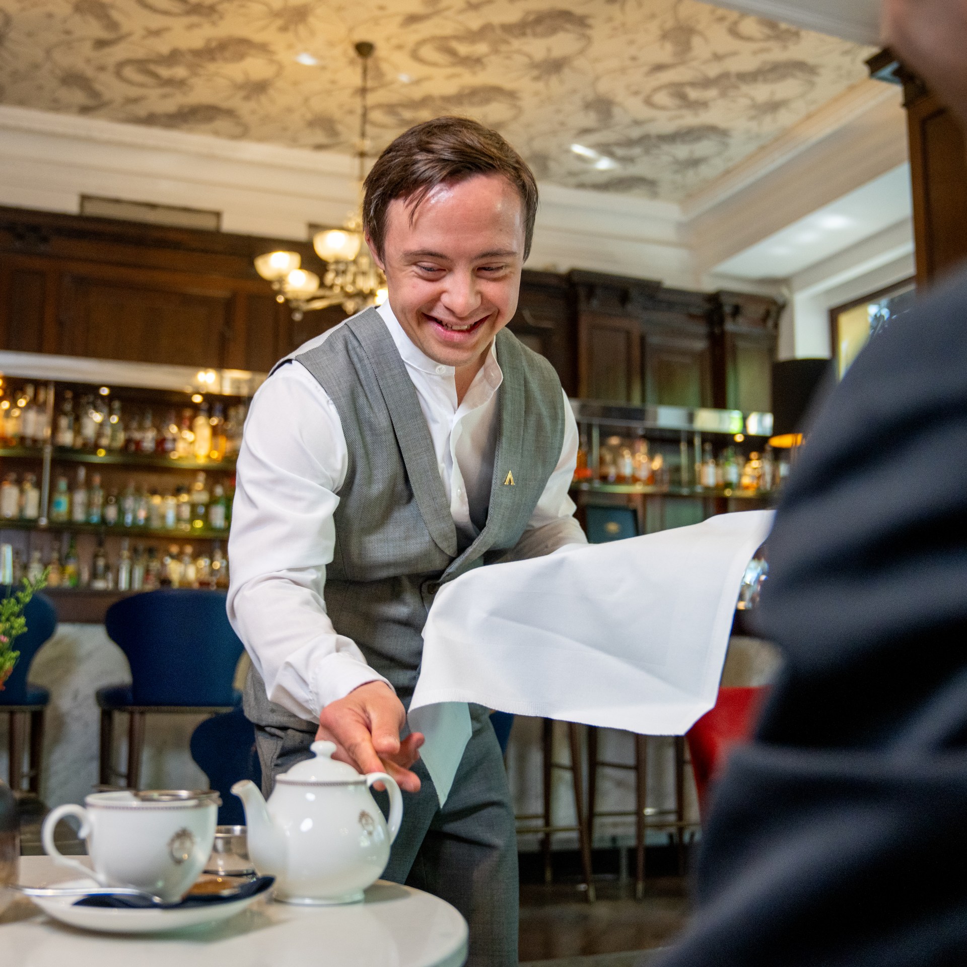 Alban placing a teapot on a table in front of a guest