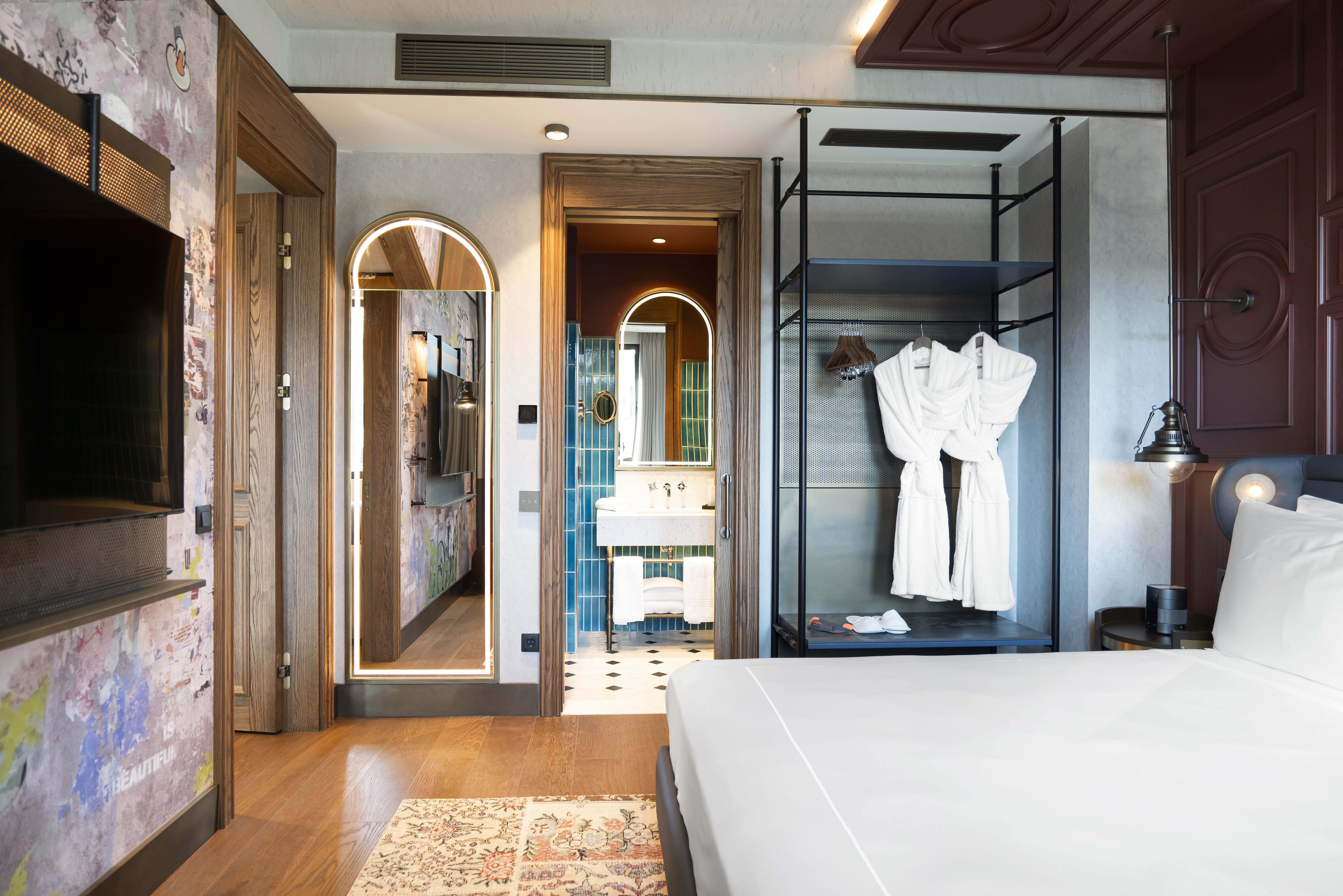 A room with bed, tv, clothes rail with roves hung up, and bathroom in the background