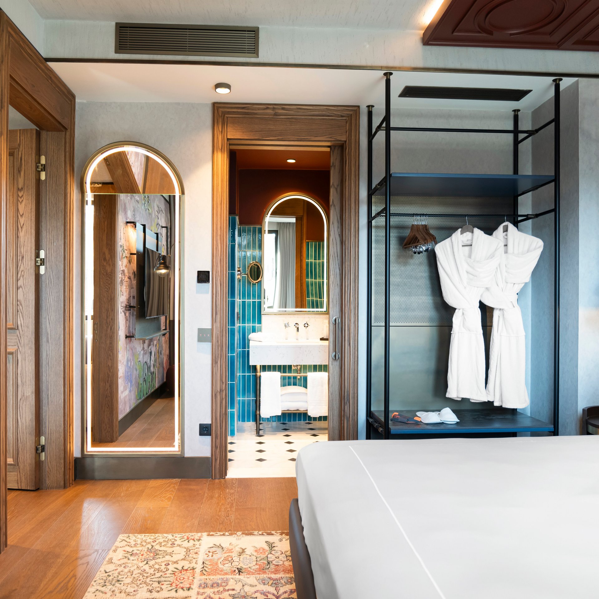 A room with bed, tv, clothes rail with roves hung up, and bathroom in the background