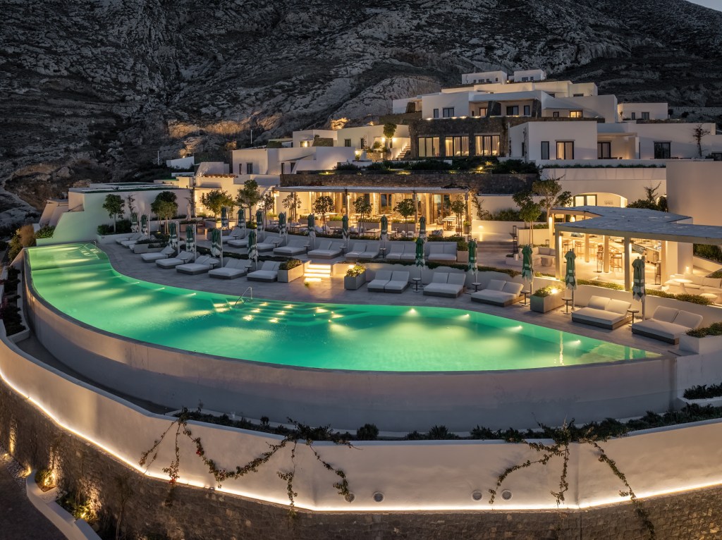 The pool lit up at night, surrounded by pool loungers