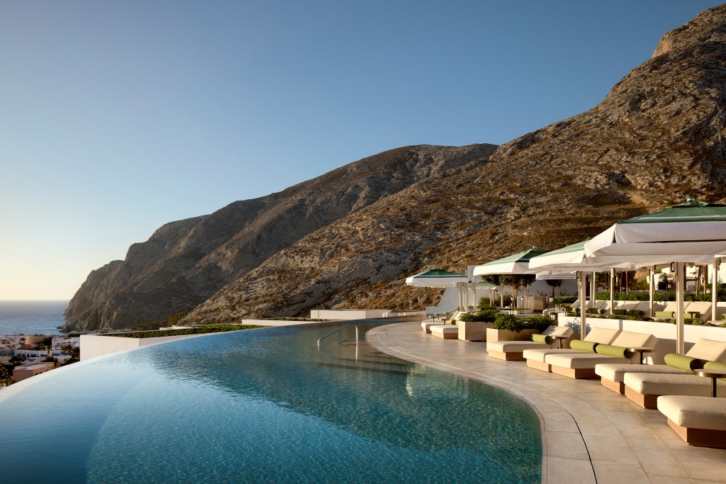 Infinity pool with loungers and umbrellas, looking out to the water, mountain in the background