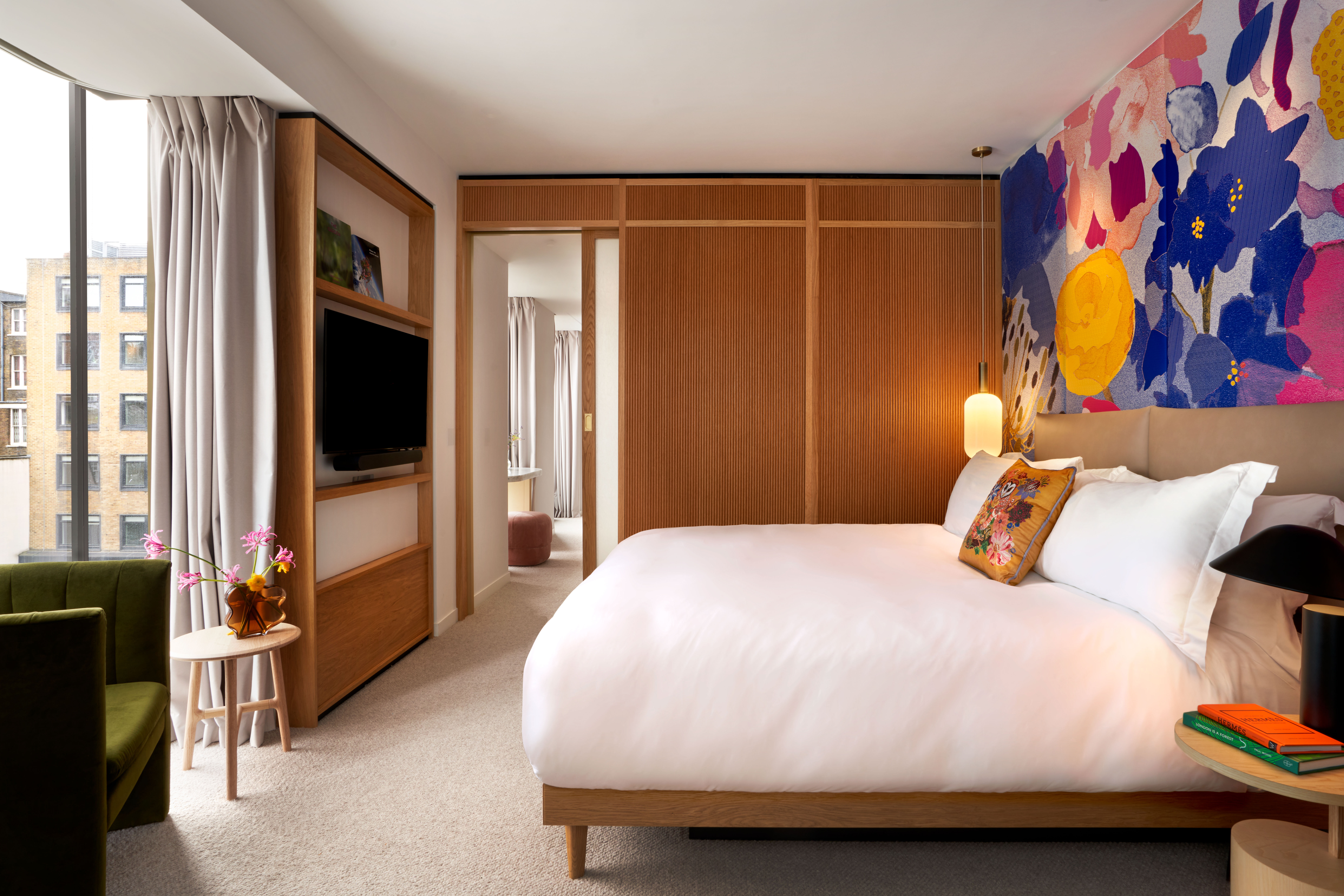 A room in guest suite with bed, chair, and tv, and another space in the background with a door between