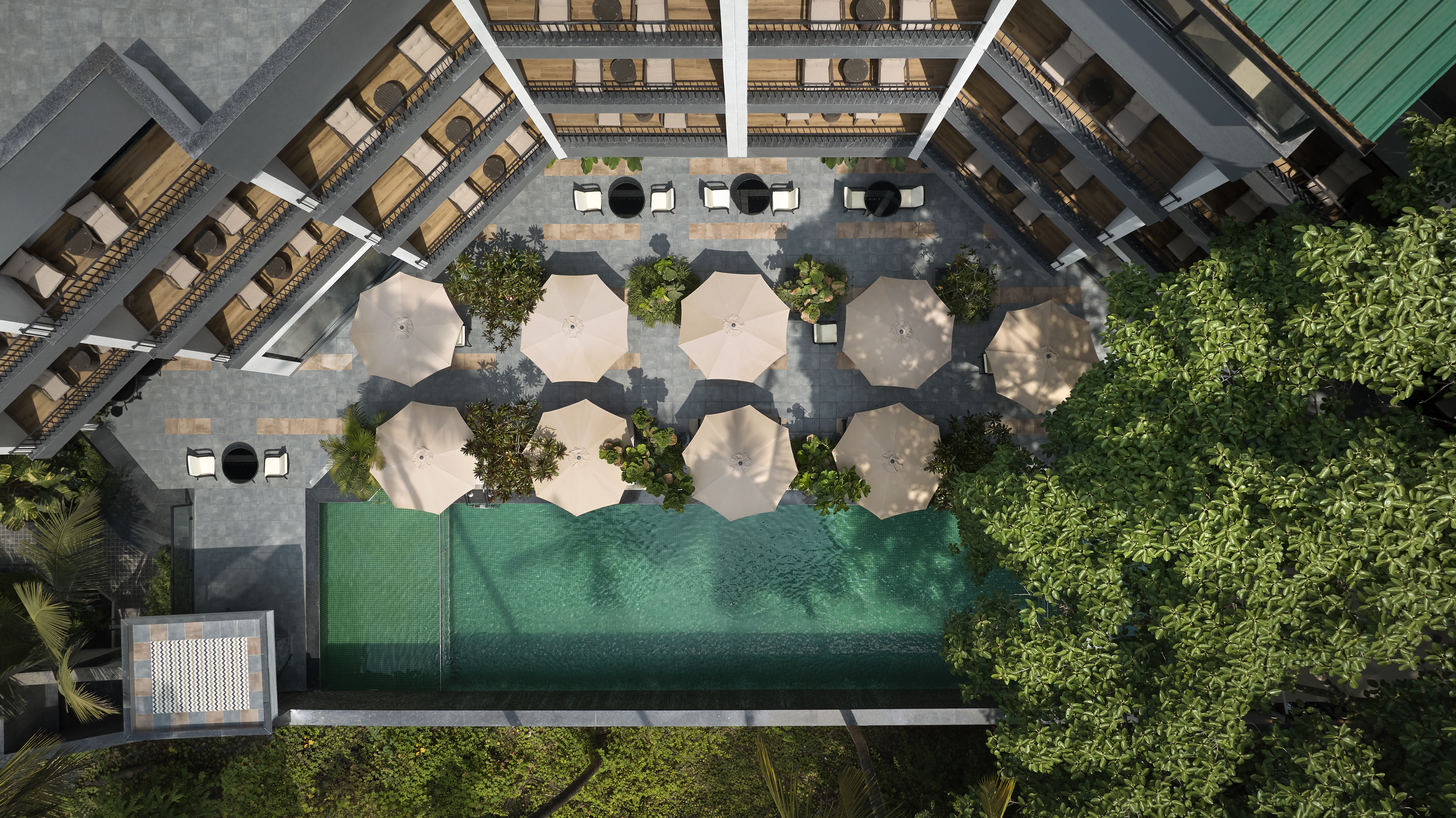Aerial view of a rectangular swimming pool surrounded by umbrellas, lounge chairs, and greenery in a modern hotel courtyard at the Spark by Hilton Goa Calangute.
