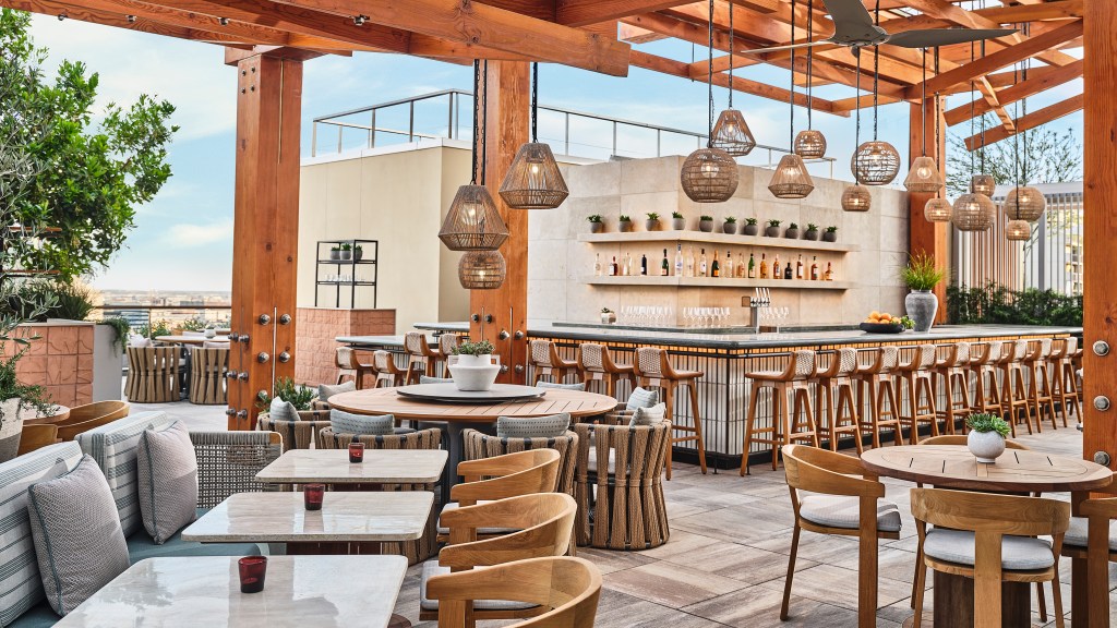 Conrad Los Angeles Agua Viva - outdoor rooftop restaurant with wood accents, variety of tables and chairs, bar area, plants, hanging light fixtures above bar