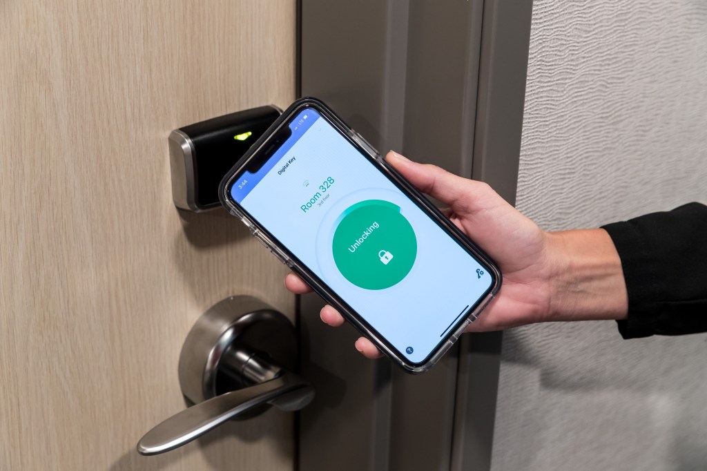 Person holding a phone with Hilton Digital Key activated and opening a hotel room door