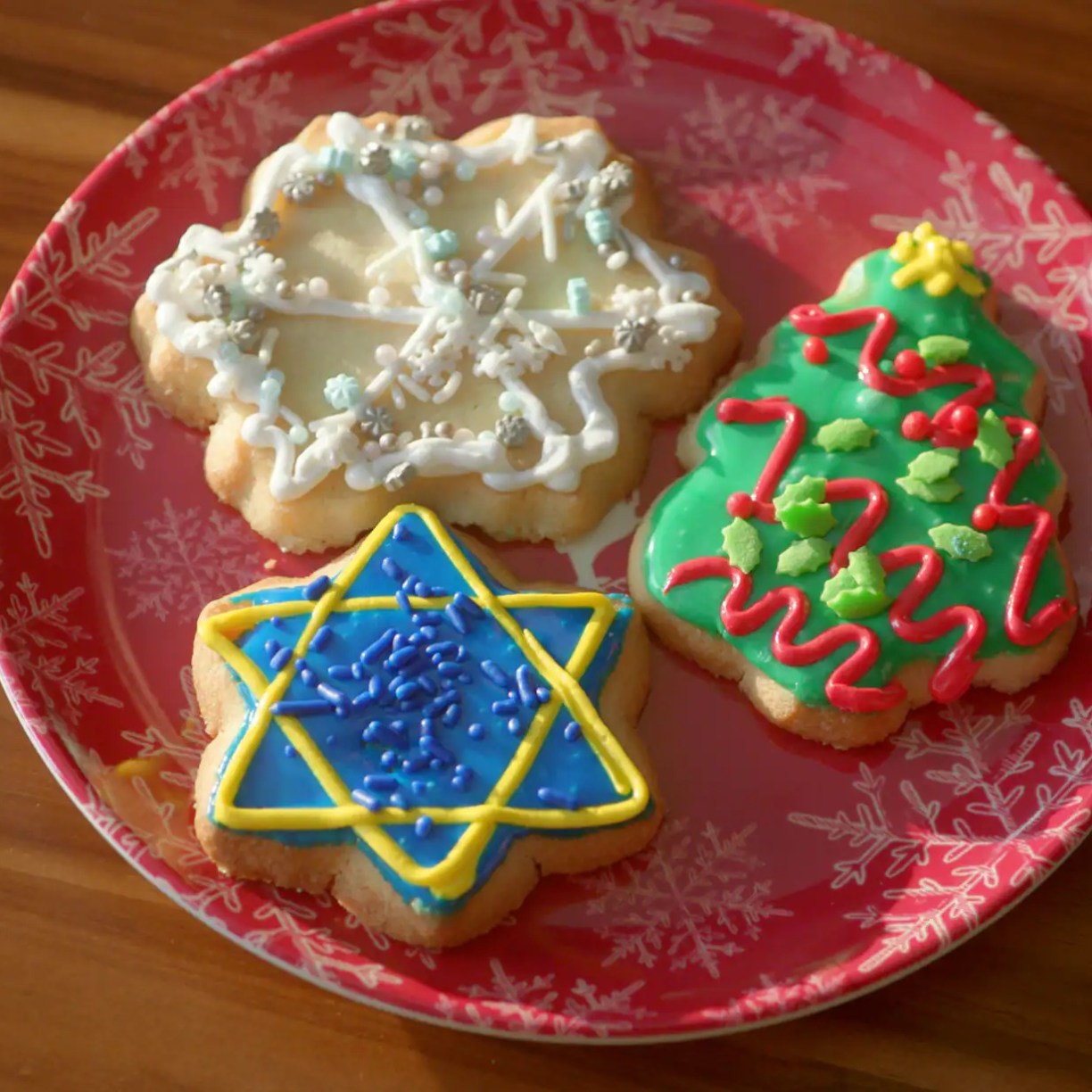 three sugar cookies decorated for the holidays including a snowflake, christmas tree and star of david