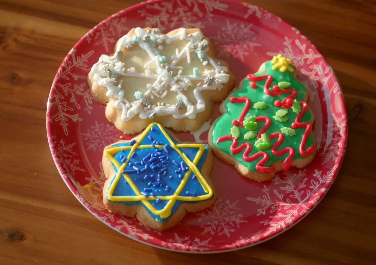 three sugar cookies decorated for the holidays including a snowflake, christmas tree and star of david