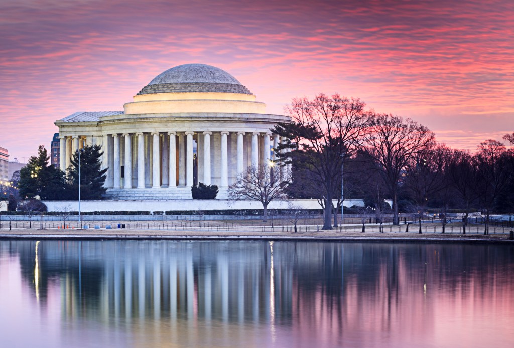 Side View of Thomas Jefferson Memorial in Washington DC under a pink sky sunrise reflecting in the water of the Tidal Basin in winter.