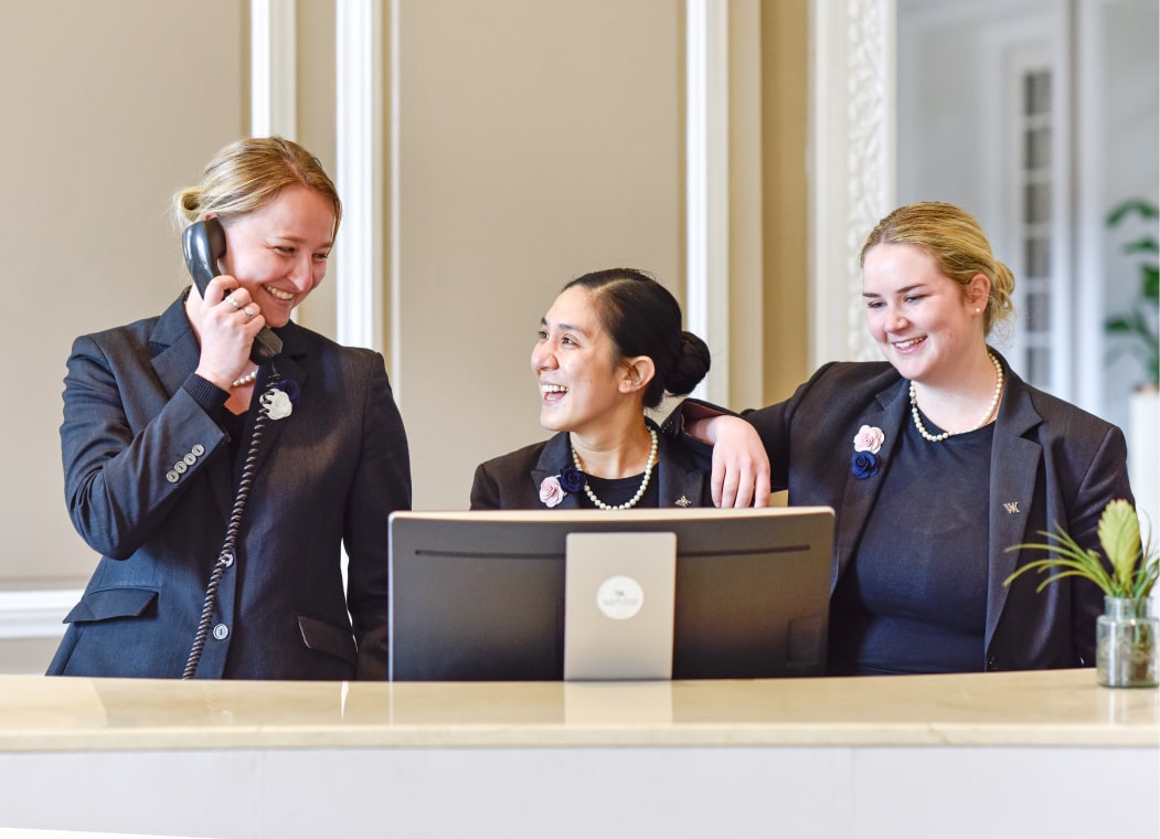 3 Hilton employees smiling at eachother at the front desk.