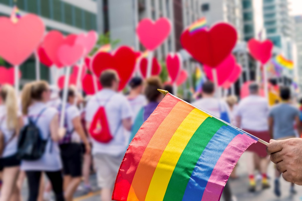 Rainbow flag in front of Pride participants holding hearts