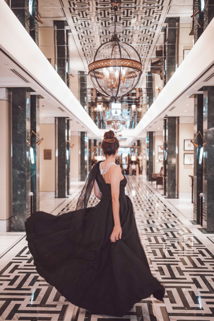 Woman in a black dress walking through lobby; Waldorf Astoria