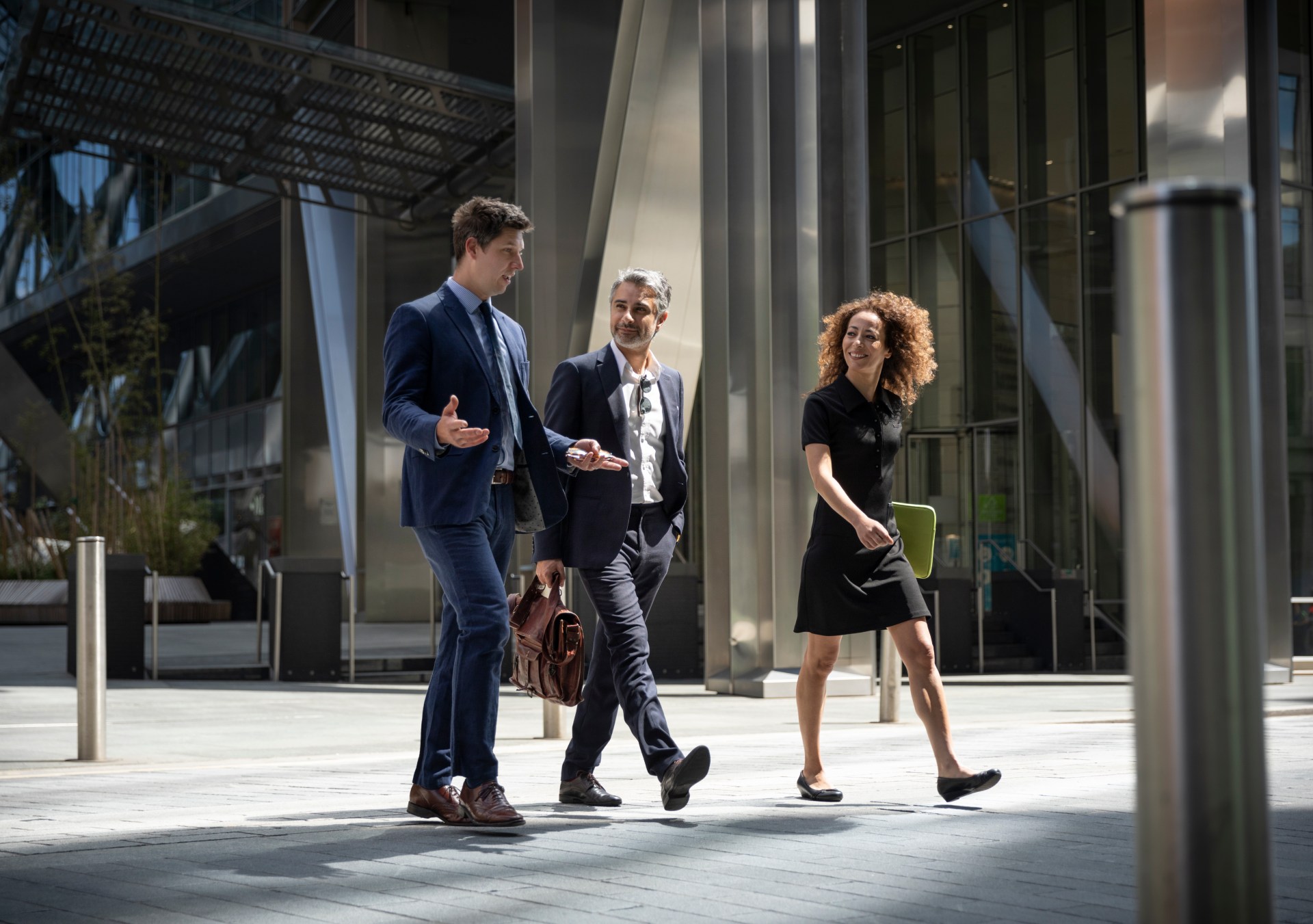 Three coworkers walking on city street with laptop discussing project