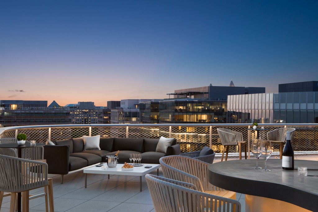 Conrad Washington DC - Rooftop Lounge, bar, wine glasses and bottles, chairs, bar seating, couch and table at sunset