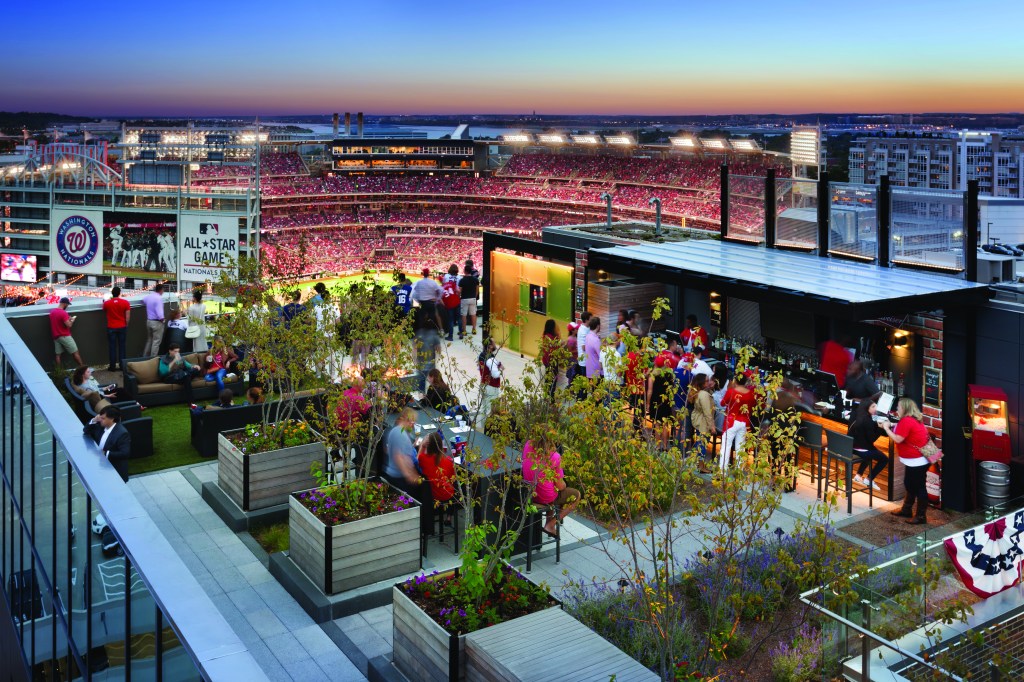 Hampton Navy Yard Rooftop bar, view of baseball stadium, people at bar, people sitting at tables and couches, people watching a baseball game from the rooftop