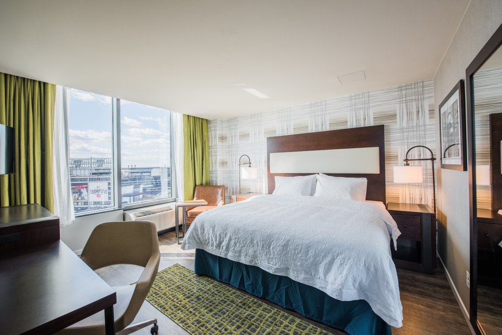 Hampton Navy Yard single queen bed room, bed, lamp, chairs, desk, side tables, curtains, air conditioner, view of baseball stadium