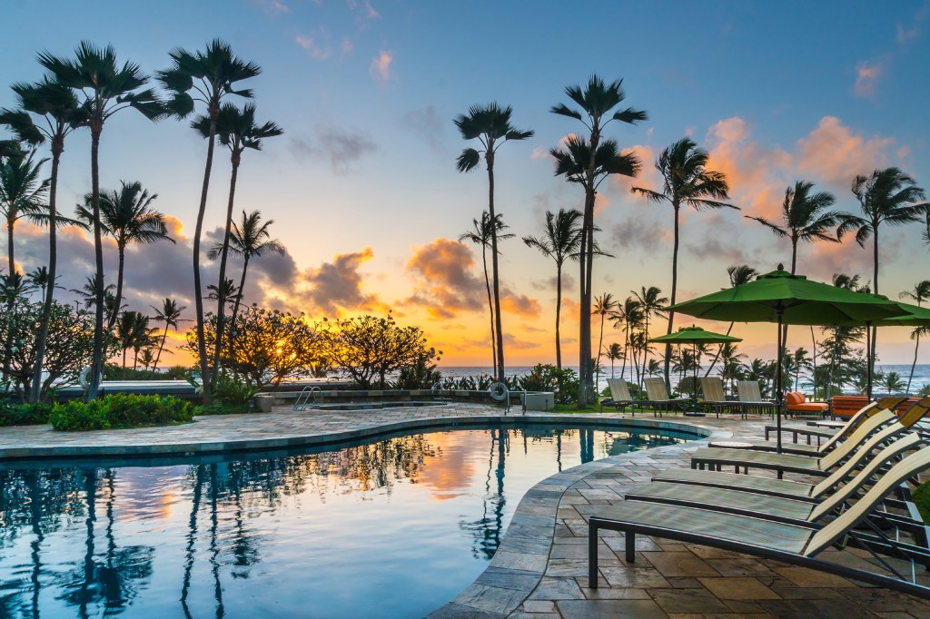 Hilton Garden Inn Kauai Wailua Bay - Pool, lounge chairs, beach umbrellas, palm trees, ocean view at sunset