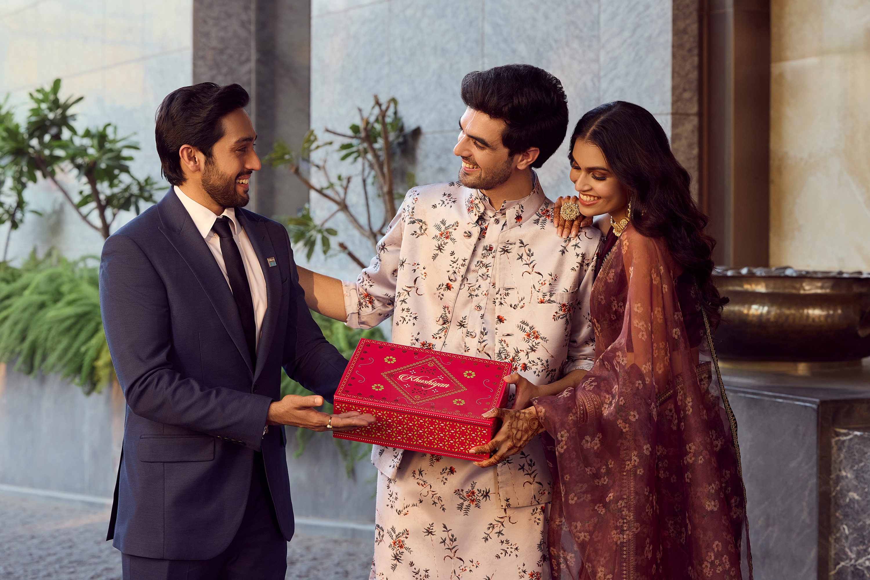 man and woman receiving red and gold gift box from man in a suit
