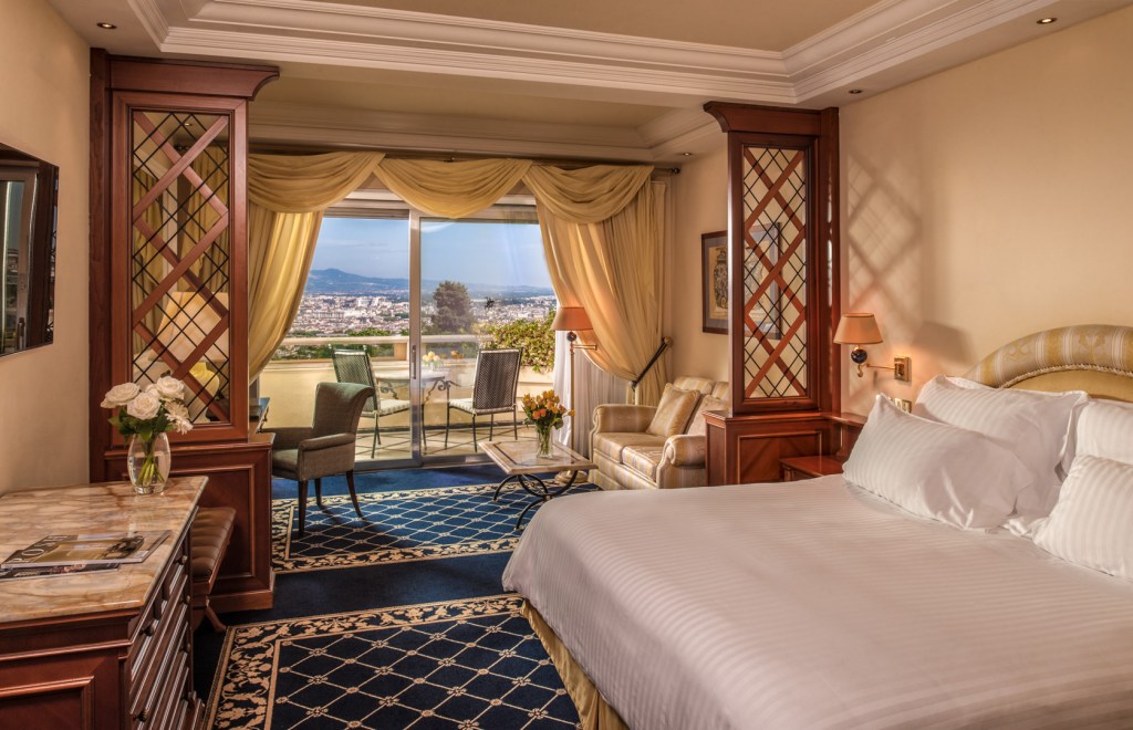 Rome Cavalieri, A Waldorf Astoria Hotel - King Deluxe Premium Rome View - bed, table, sconces, chairs, couch, coffee table, vase with flowers, desk and chair, lamps, blacony, outdoor chairs and table over looking city