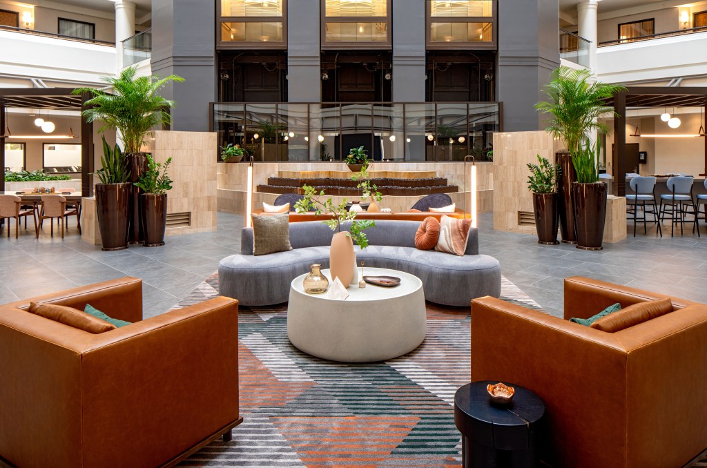 DoubleTree Suites by Hilton Salt Lake City Downtown - Lobby, sofas, chairs coffee and end tables, view of water fountain and elevators, plants and tables and chairs on both sides of the fountain