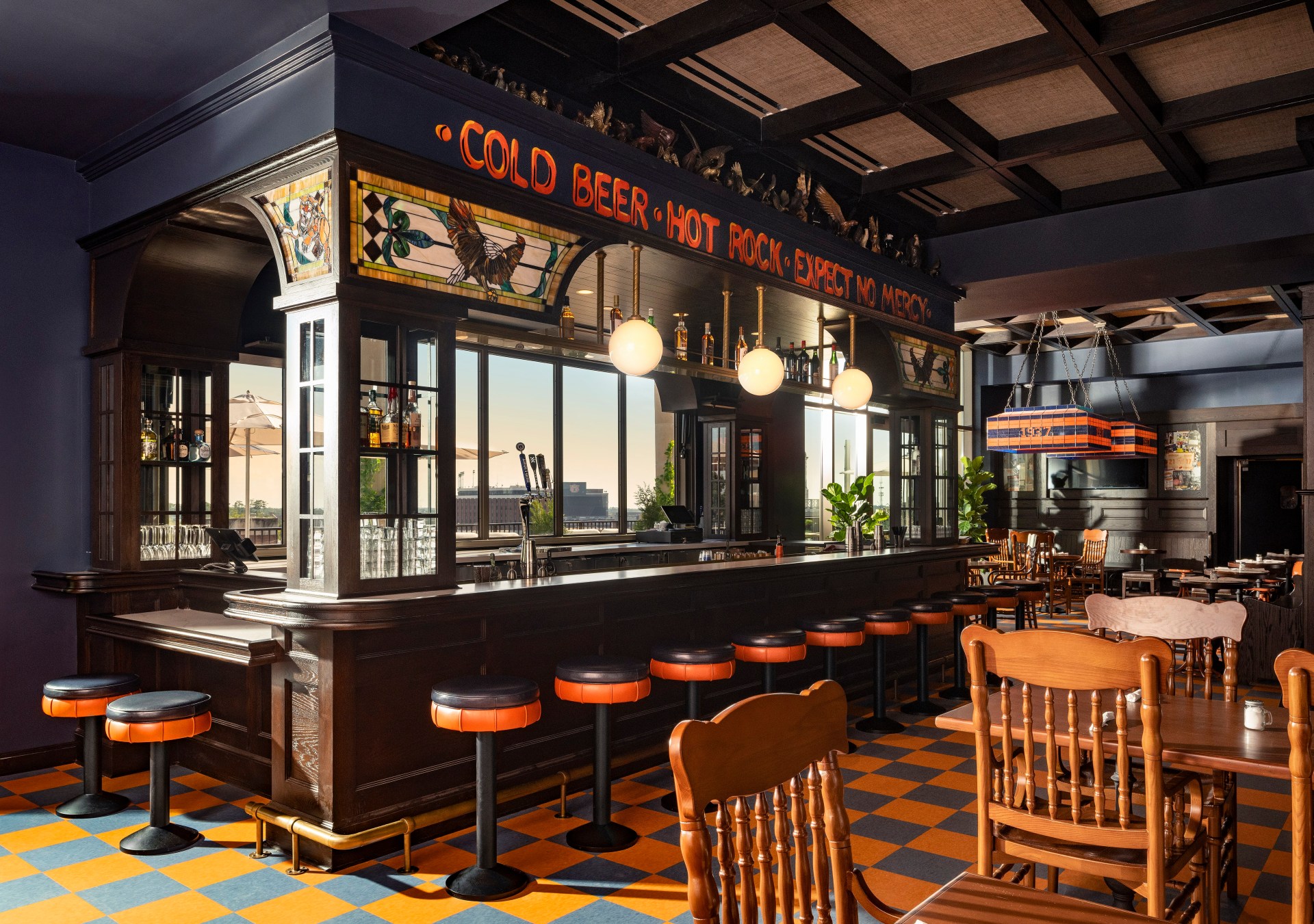Graduate by Hilton Auburn, AL - War Eagle Supper Club - Central Bar Area with "Cold Beer Hot Rock Expect No Mercy" written above the bar, orange and navy accents throughout