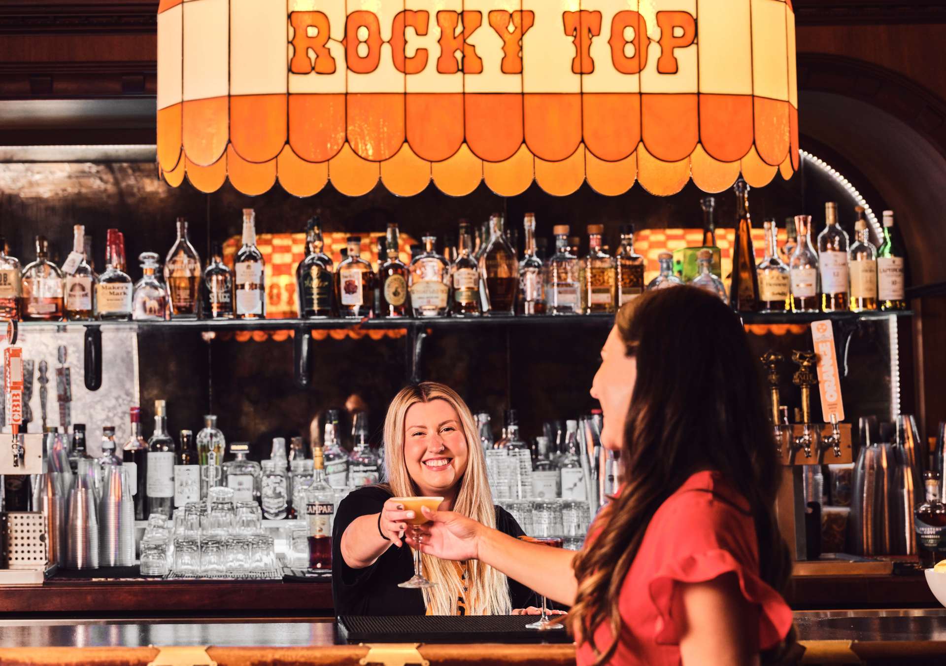 Graduate by Hilton Knoxville - Saloon 16 - bartender hands a drink to woman across the bar, with large colorful "Rocky Top" light fixture above