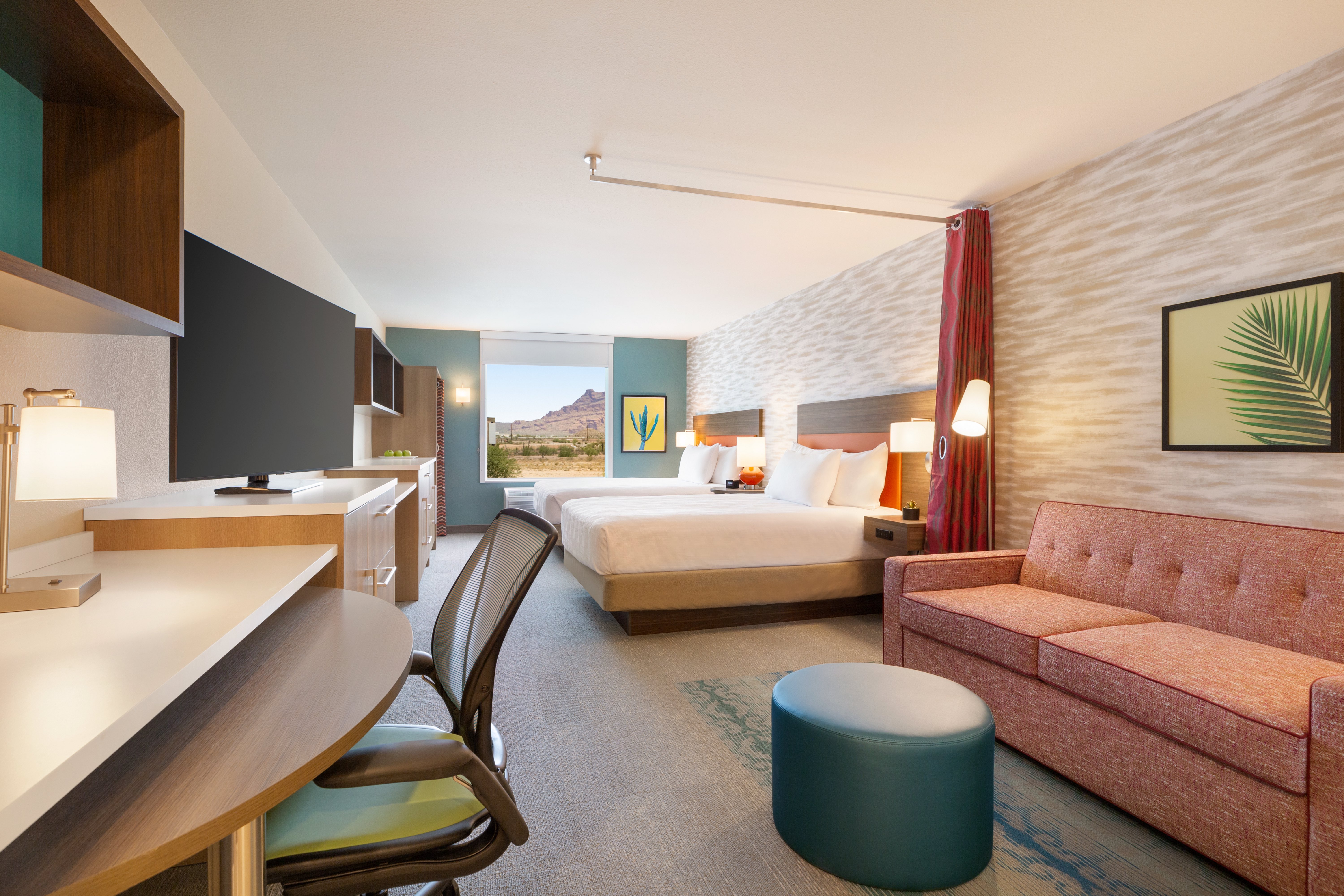 Guest room with sofa, desk and chair, television, two beds, and window looking out at desert scenery at Home2 Suites by Hilton Mesa Longbow