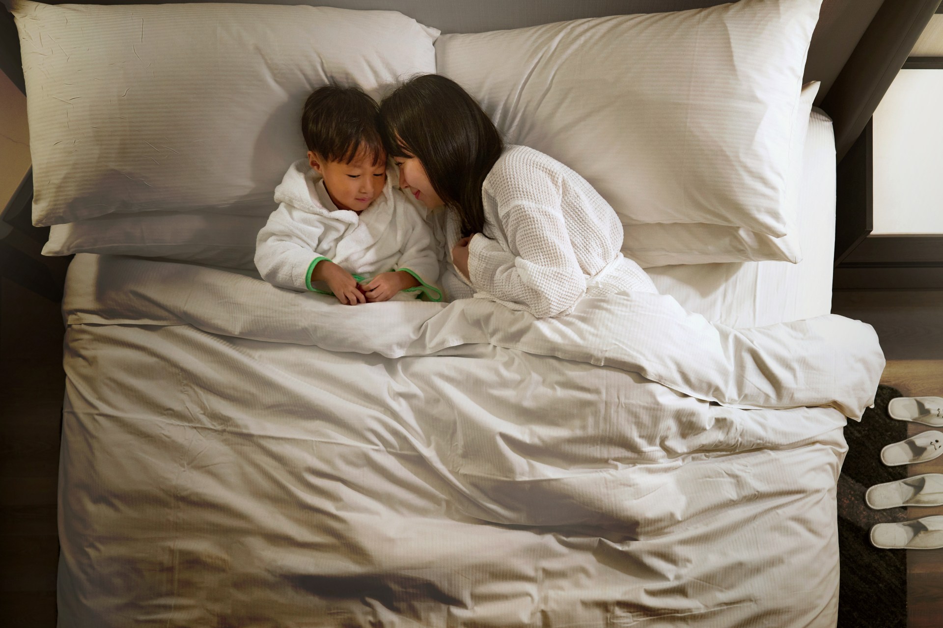 Mother and young child cuddling in bed with hotel robes