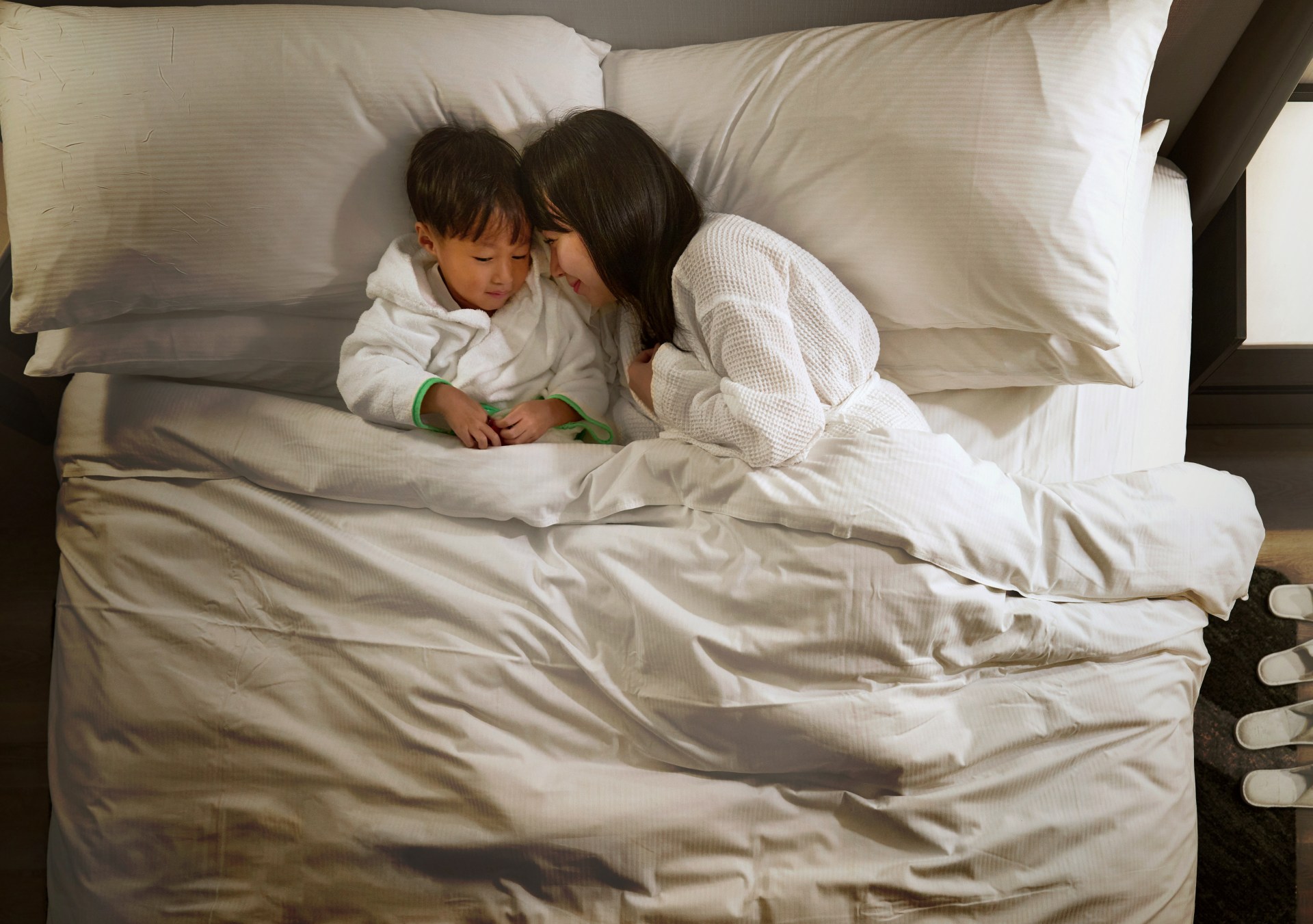 Mother and young child cuddling in bed with hotel robes