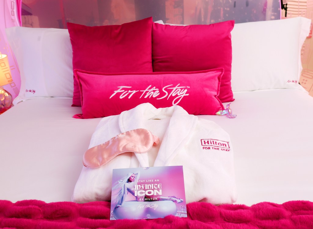 Stay Like an Infinite Icon Themed Suites at Beverly Hilton - Custom Bedding featuring hot pink pillows with &quot;For the Stay&quot;, a Hilton For The Stay robe and a light pink eye mask - Photo Credit: Rich Polk/Getty Images for Hilton